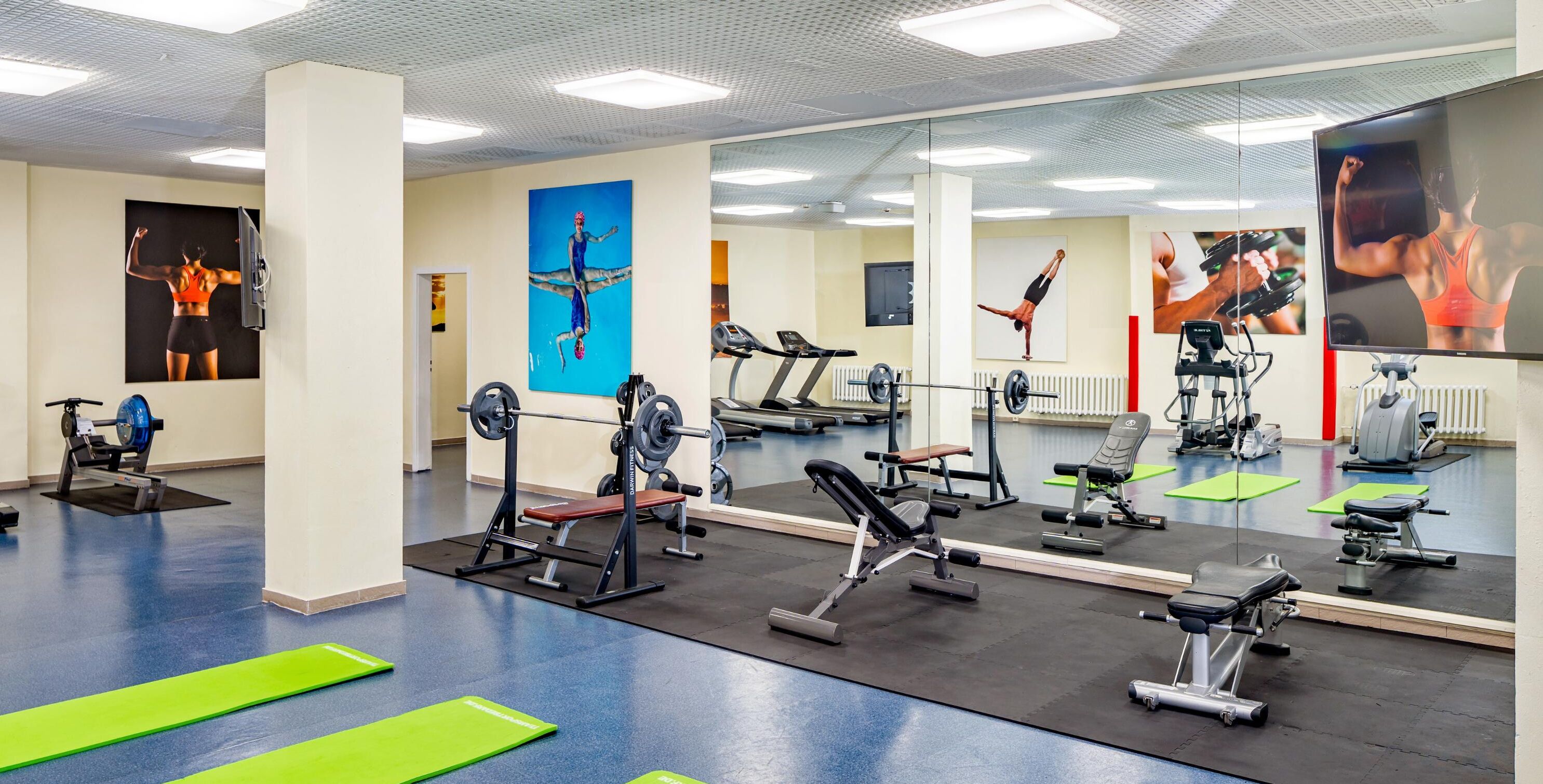 Ett gym med olika typer av träningsredskap, speglar och gröna mattor.