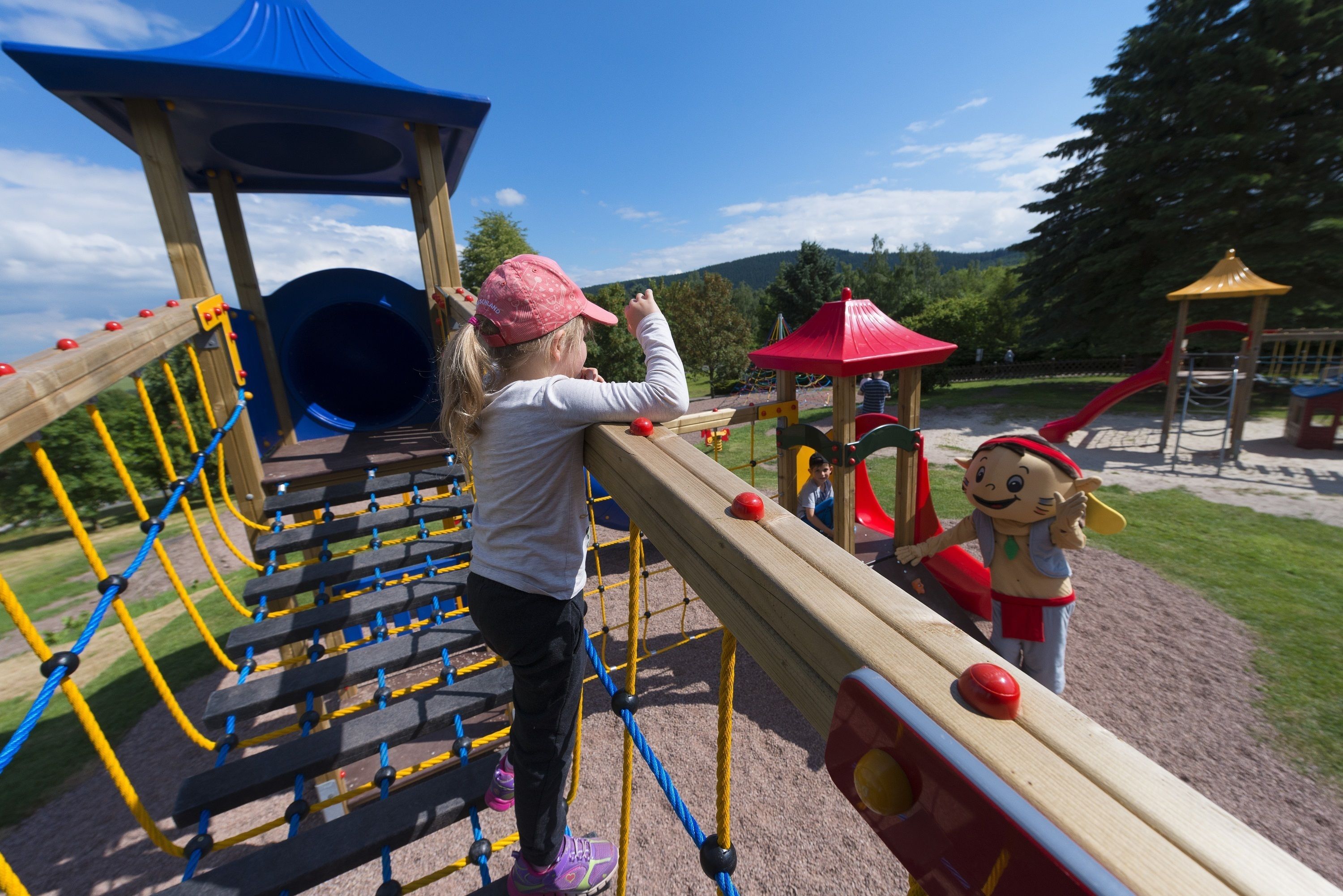 A playground with a climbing structure, a slide, and a red umbrella.