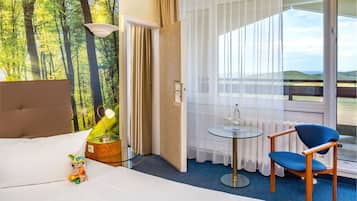 Habitación de hotel con cama, una mesita con silla, una lámpara y vistas al exterior.