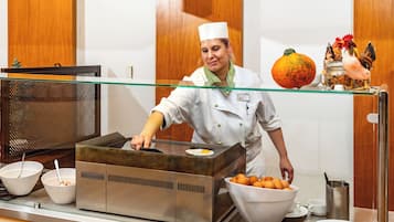 Um chef numa cozinha com estação de cozinha em aço inoxidável, tigelas com ingredientes e um galo decorativo numa prateleira.