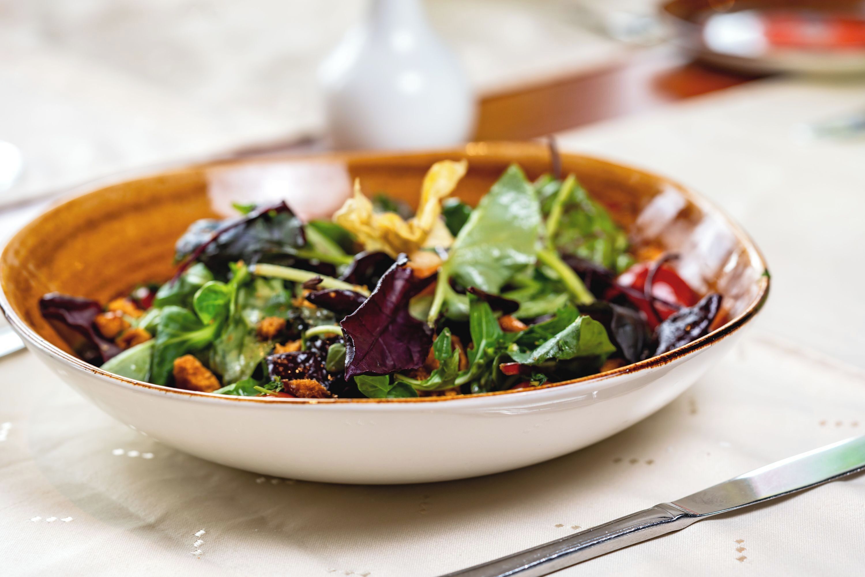 A bowl of salad with various greens and nuts on a white plate.