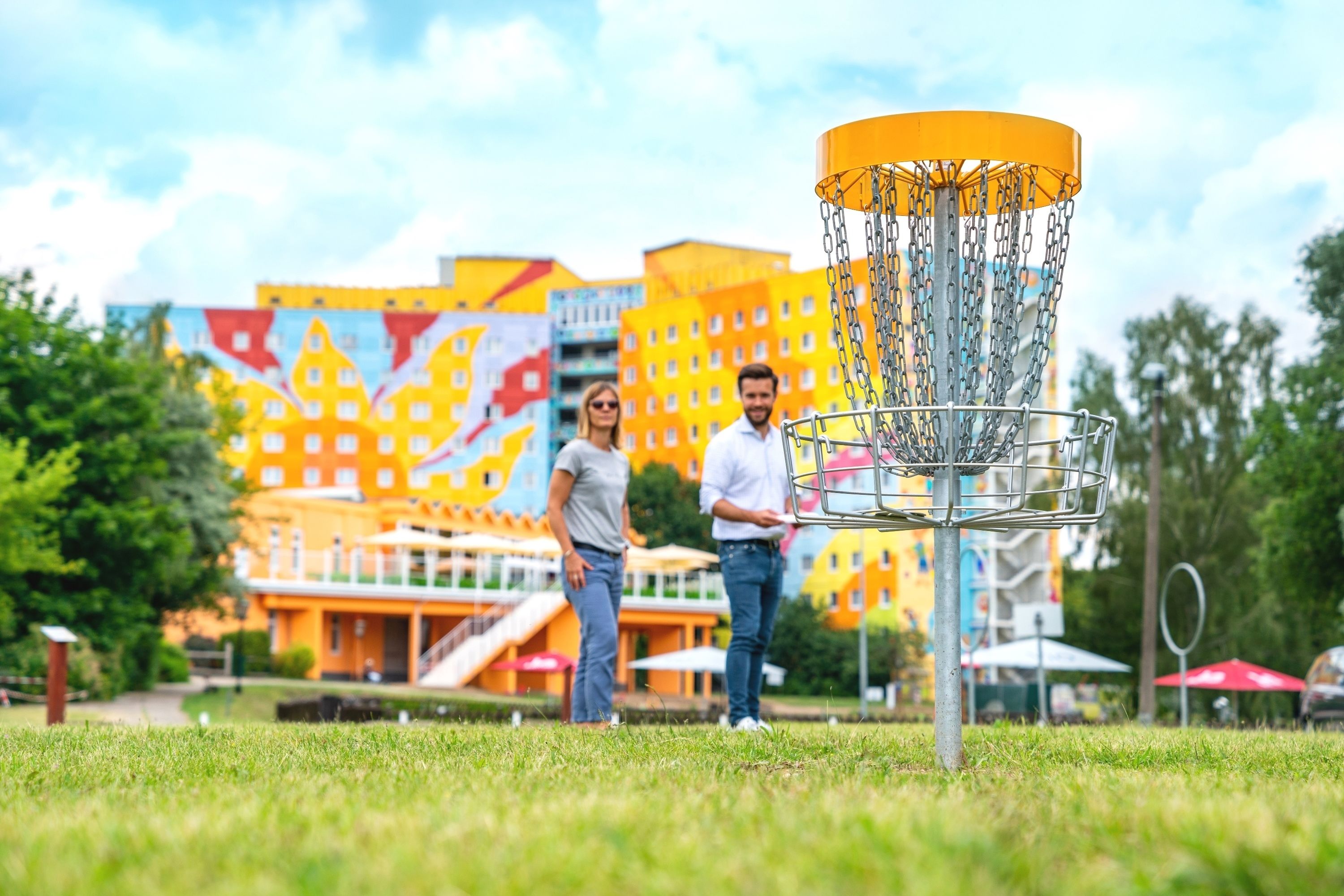 Een frisbeebaankje in een park, met kleurrijke gebouwen op de achtergrond.