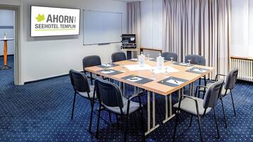 Un salón de conferencias con una larga mesa, seis sillas, una pantalla de proyector y un cartel que dice "AHORN SEEHOTEL TEMPLIN".