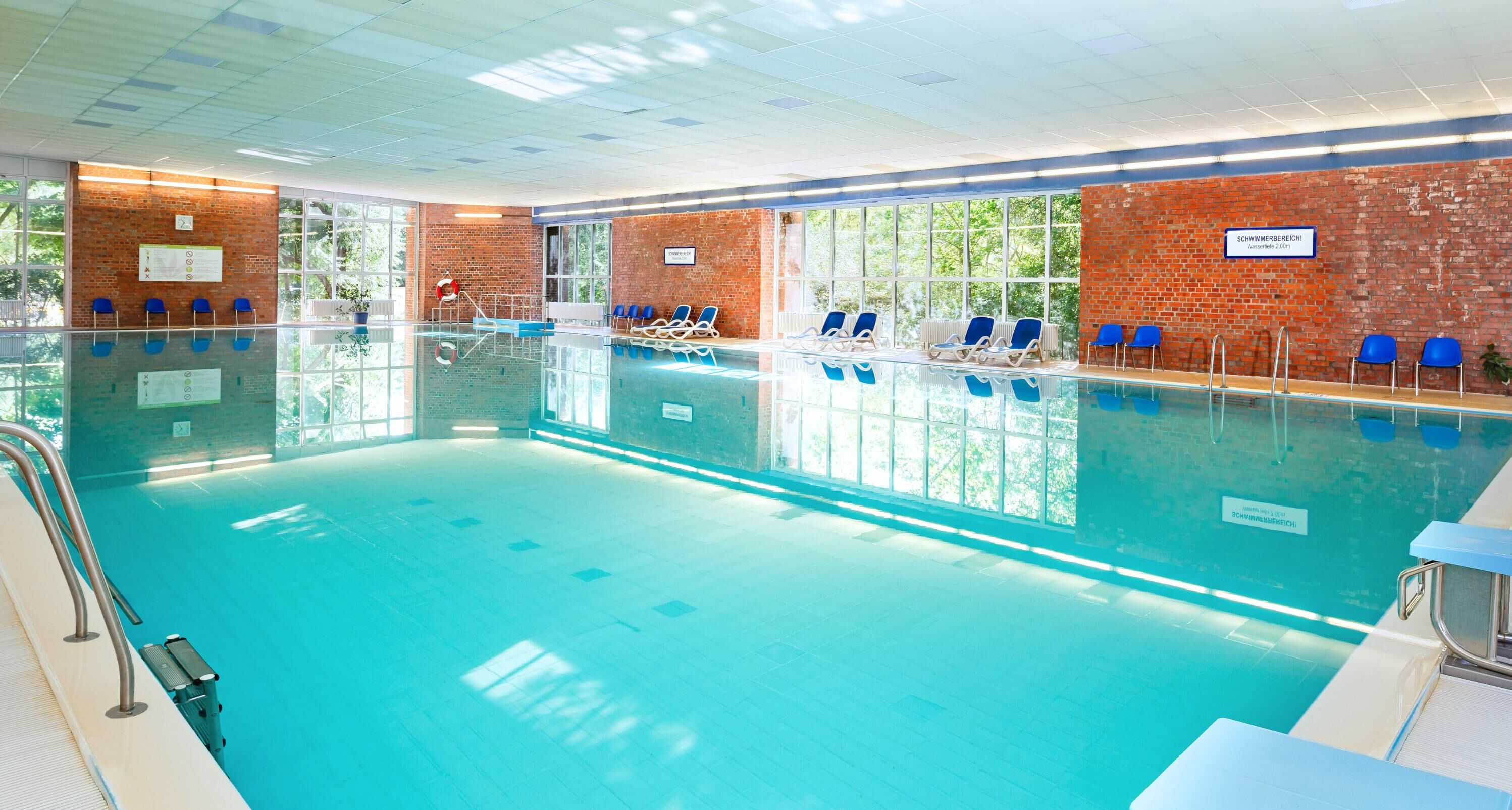 An indoor swimming pool with clear blue water, surrounded by brick walls and large windows.