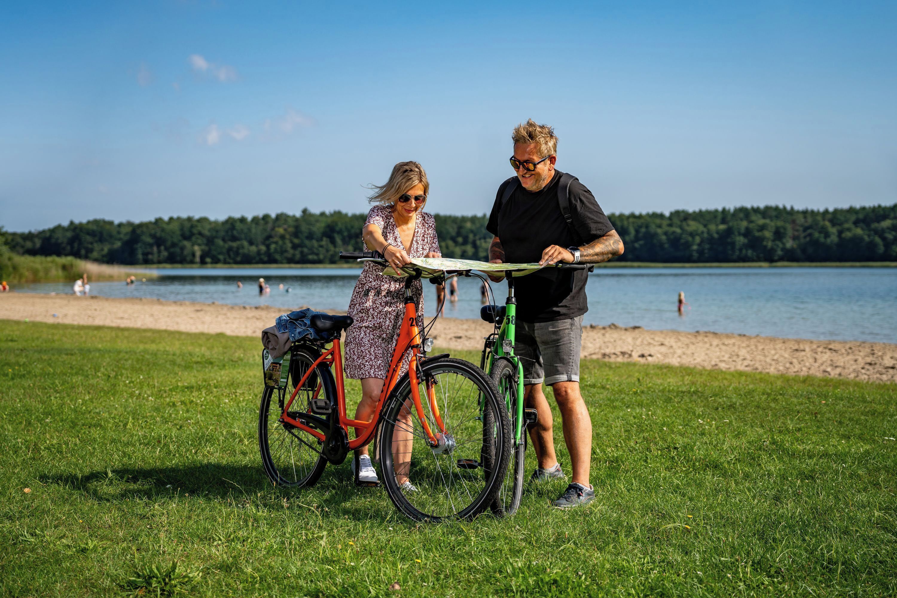 A couple standing on a grassy area near a lake with bicycles.