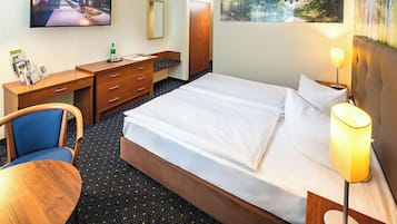 A hotel room with a bed, a desk with a chair, a television, and a painting on the wall.