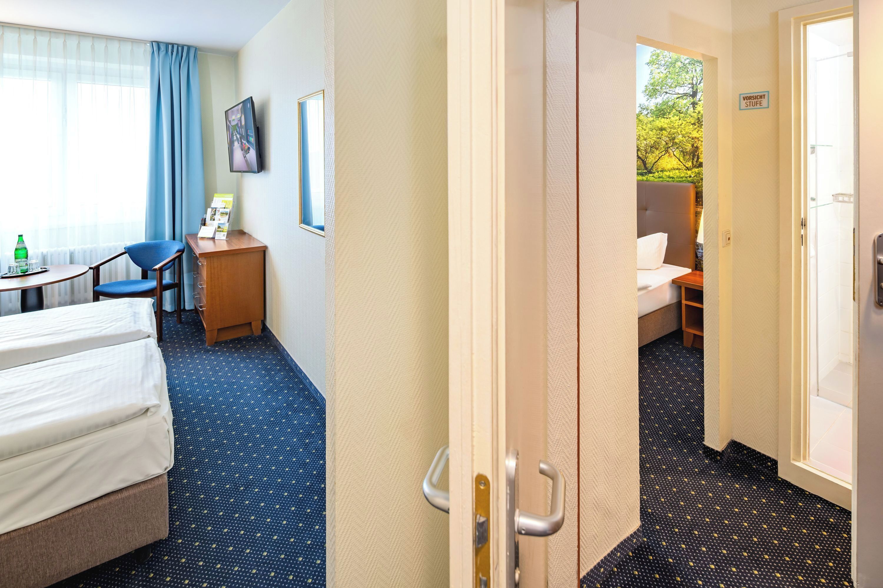 Habitación de hotel con cama, escritorio, silla y vista al exterior a través de una puerta abierta.