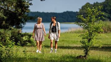 Two people walking in a grassy area with trees and a body of water in the background.