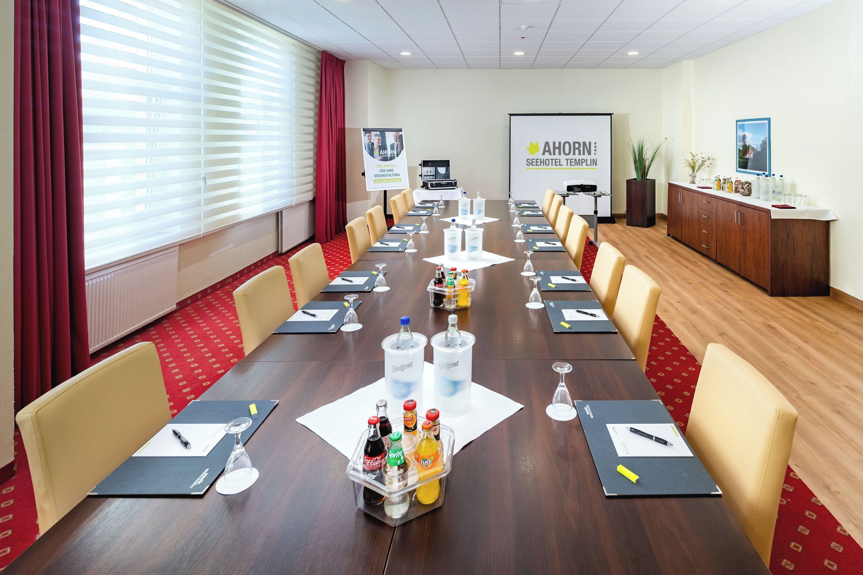 A conference room with a long table, chairs, water bottles, and a projector screen.
