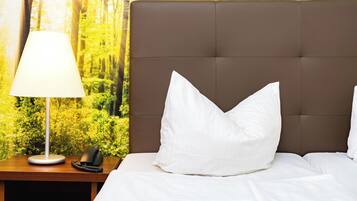 Una cama bien hecha con ropa de cama y almohadas blancas, una lámpara de noche y un teléfono sobre una mesita de madera.