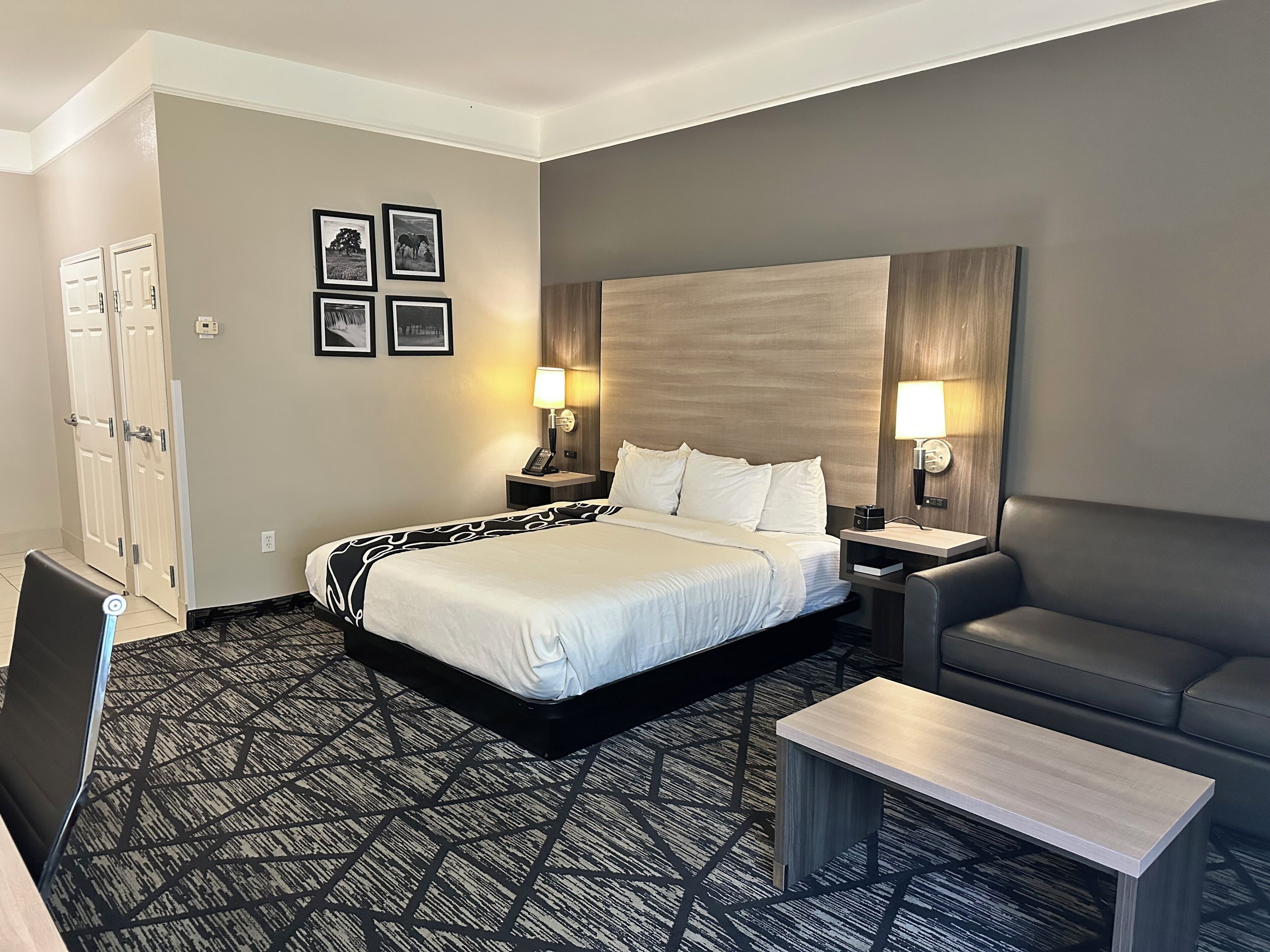 Habitación de hotel con una cama grande, dos mesitas de noche con lámparas, un sofá y una pequeña mesa.