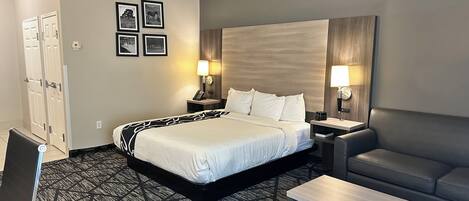 A hotel room with a large bed, two bedside tables with lamps, a sofa, and a small table.