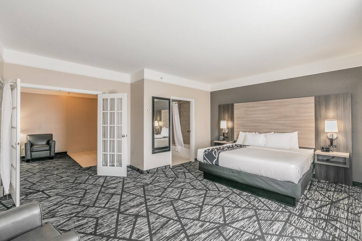 Een hotelkamer met een groot bed, een stoel, een bureau met een lamp en een spiegel.
