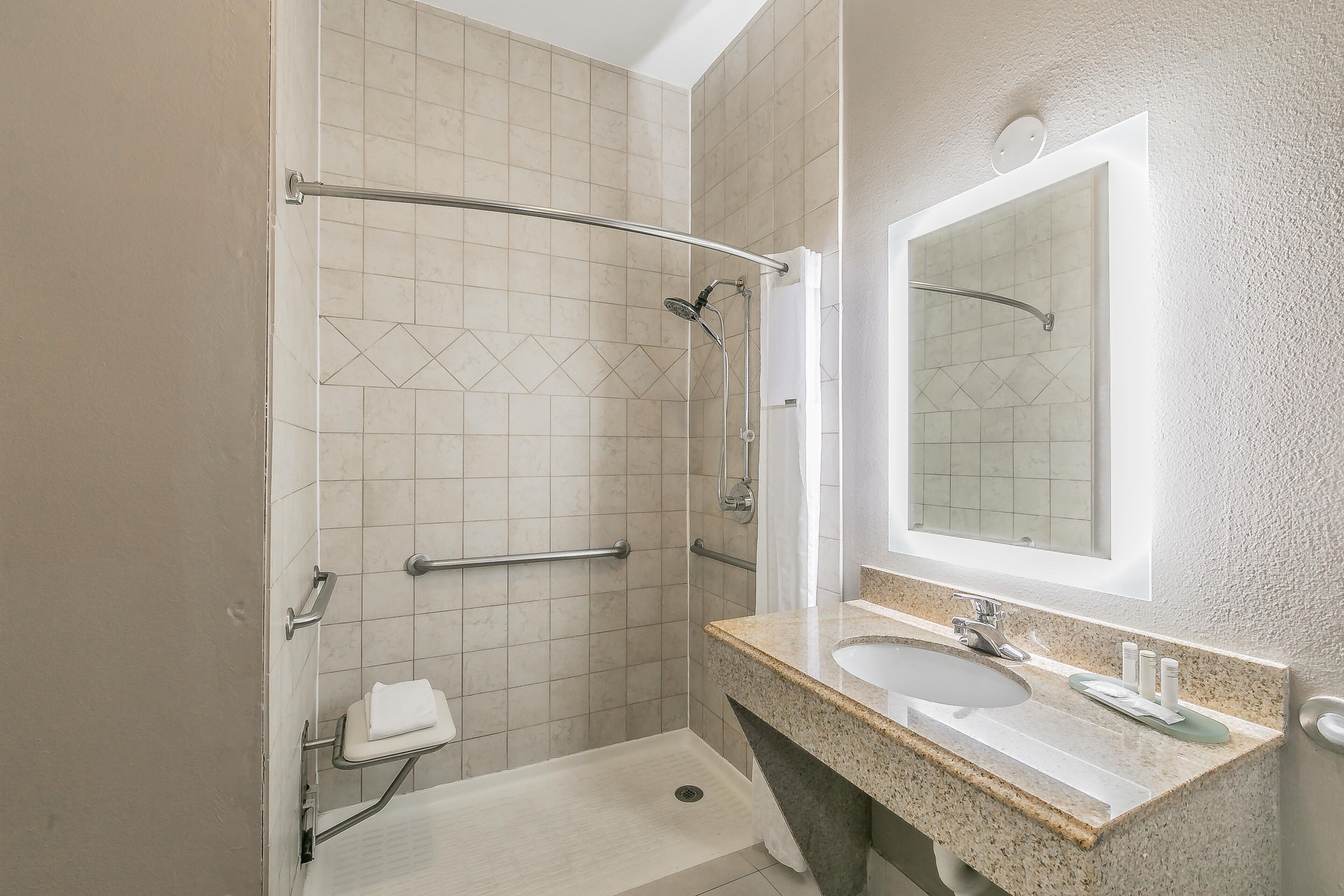Ein modernes Badezimmer mit Dusche, Haltegriffen, Waschbecken und Spiegel.