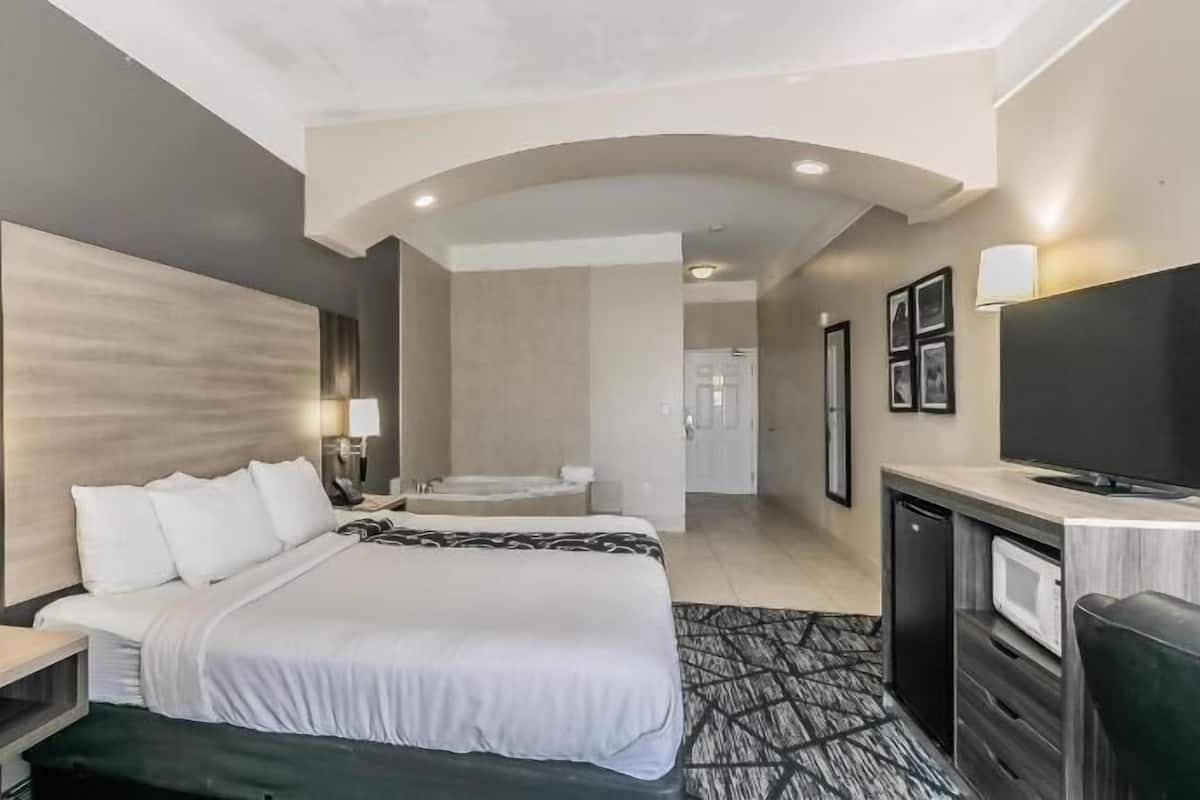 Een hotelkamer met een bed, nachtkastjes, een televisie, een bureau en een badkamer op de achtergrond.