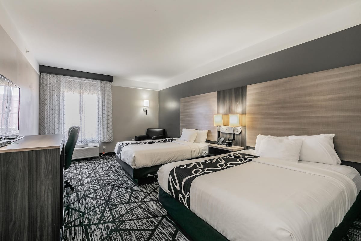 Een hotelkamer met twee bedden, een bureau, een stoel en een groot raam met gordijnen.