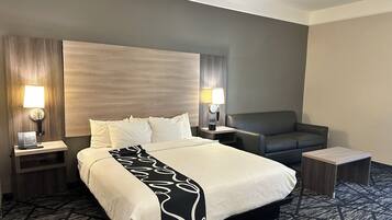 Quarto de hotel com uma cama grande, duas mesas de cabeceira, uma cadeira, uma escrivaninha e duas luminárias fixadas na parede.