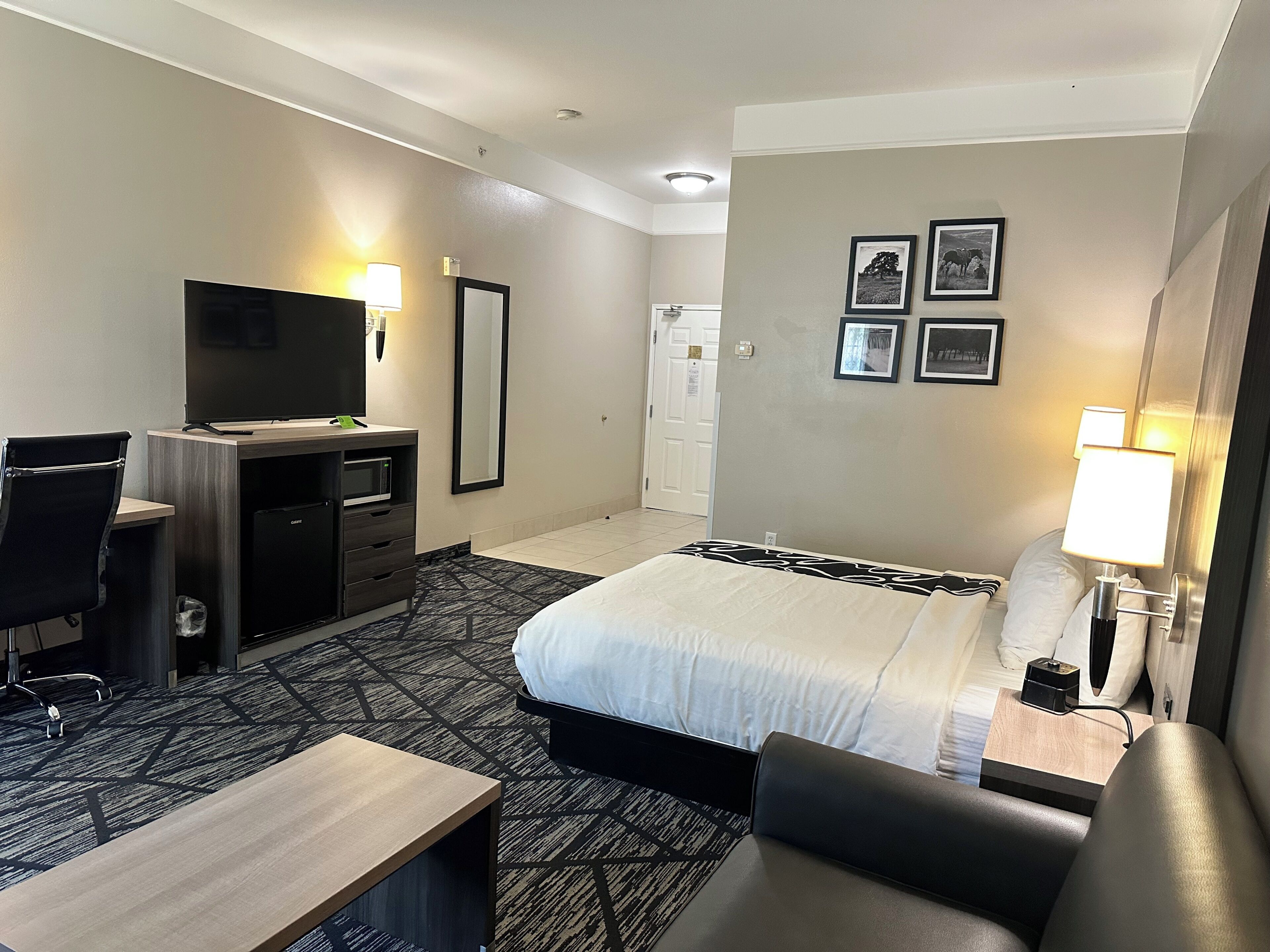 Une chambre d’hôtel équipée d’un lit, d’un bureau, d’une chaise, d’une télévision et de lampes fixées au mur.