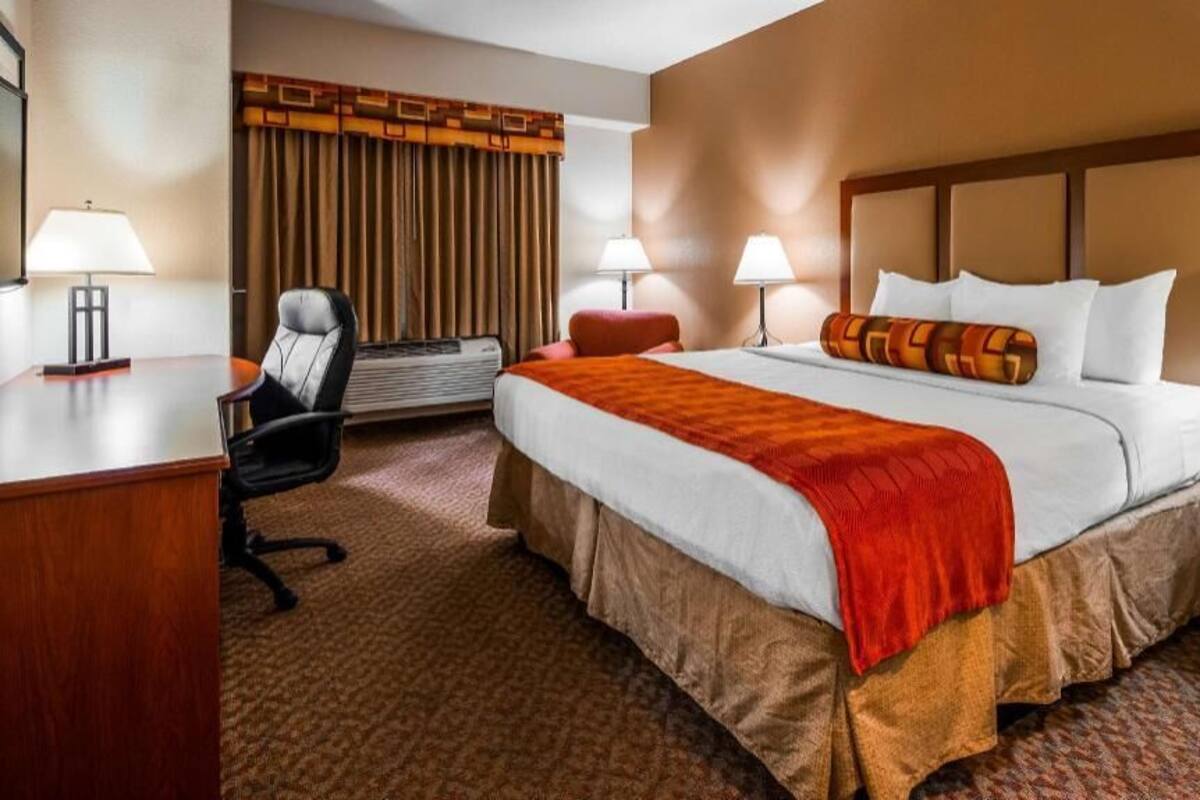 A hotel room with a bed, desk, chair, lamps, and a window with curtains.