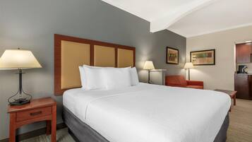 Una habitación de hotel con una cama grande, dos mesitas de noche con lámparas, un escritorio pequeño y una silla.