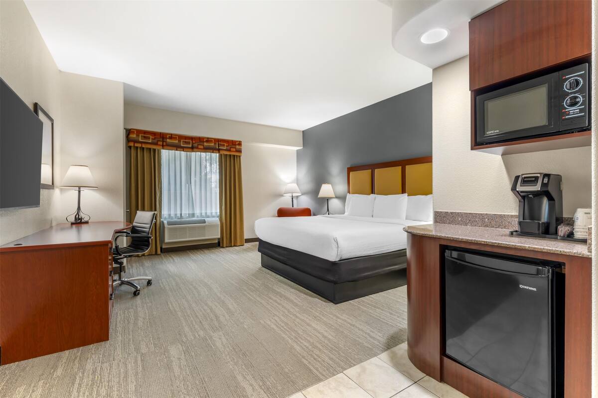 A hotel room with a bed, desk, chair, and kitchenette.