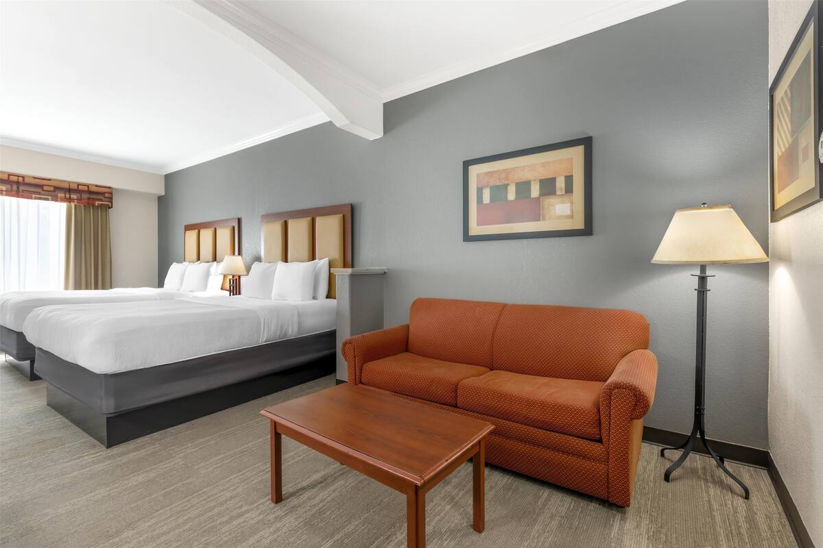A hotel room with a double bed, a sofa, a coffee table, and a floor lamp.