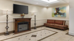 A hotel lobby with a fireplace, two floor lamps, a sofa, a flat-screen TV, and a painting on the wall.