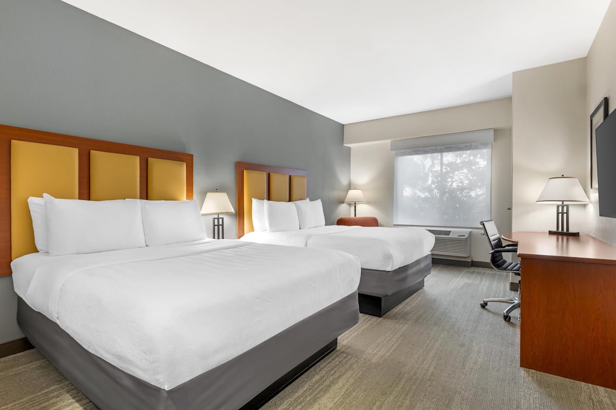 A hotel room with two beds, a desk, and a chair.