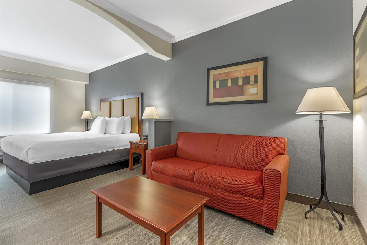 A hotel room with a bed, a red sofa, a wooden coffee table, and a floor lamp.