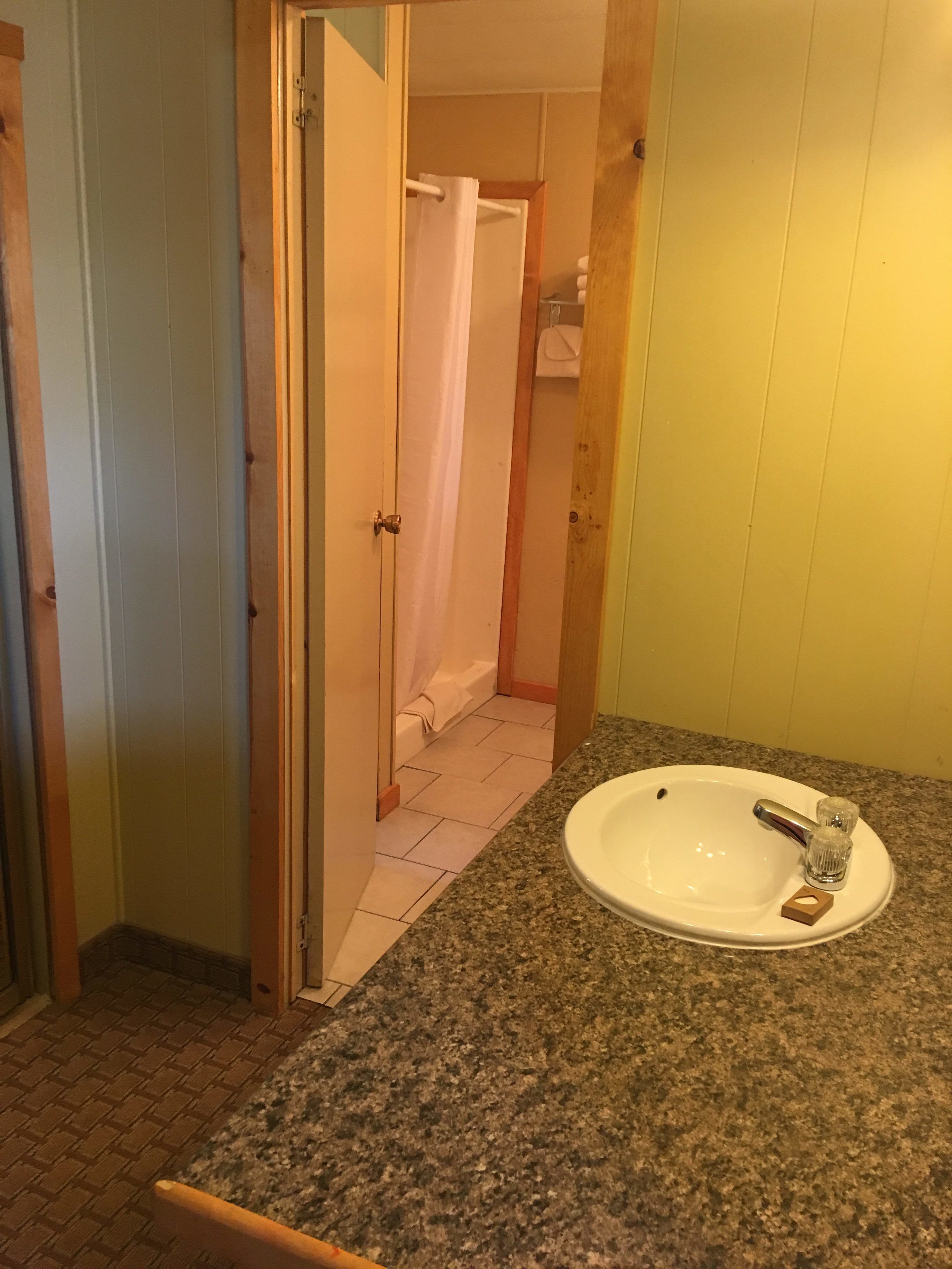 Un baño con encimera de granito, lavamanos blanco y zona de ducha.