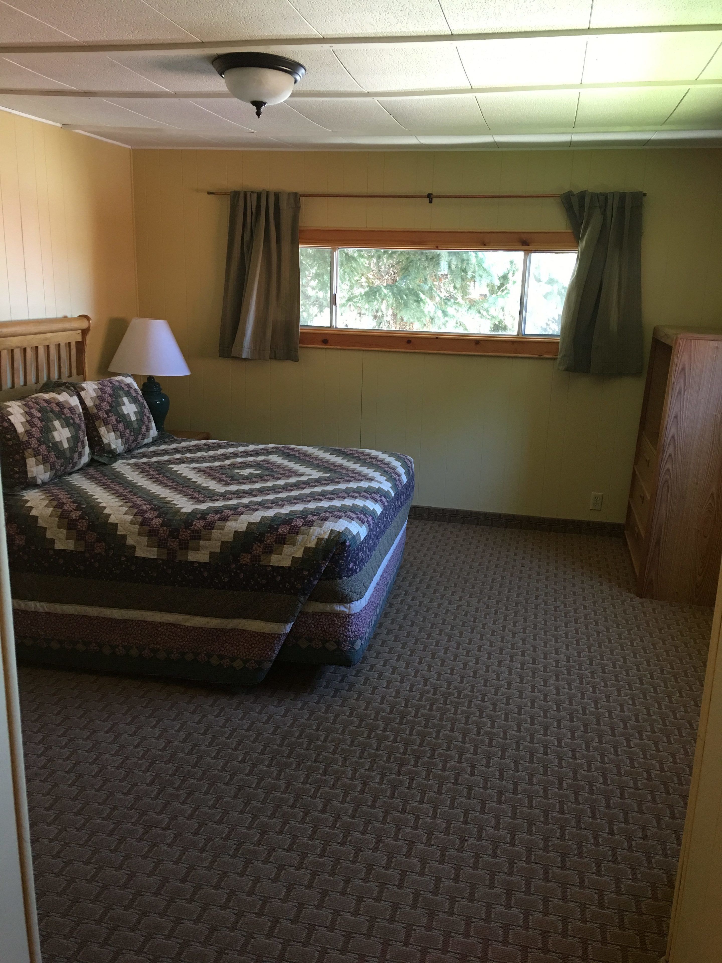 A bedroom with a bed, a window with curtains, a ceiling fan, and a lamp.