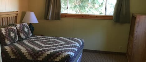 A bedroom with a bed, a window with curtains, a ceiling fan, and a lamp.