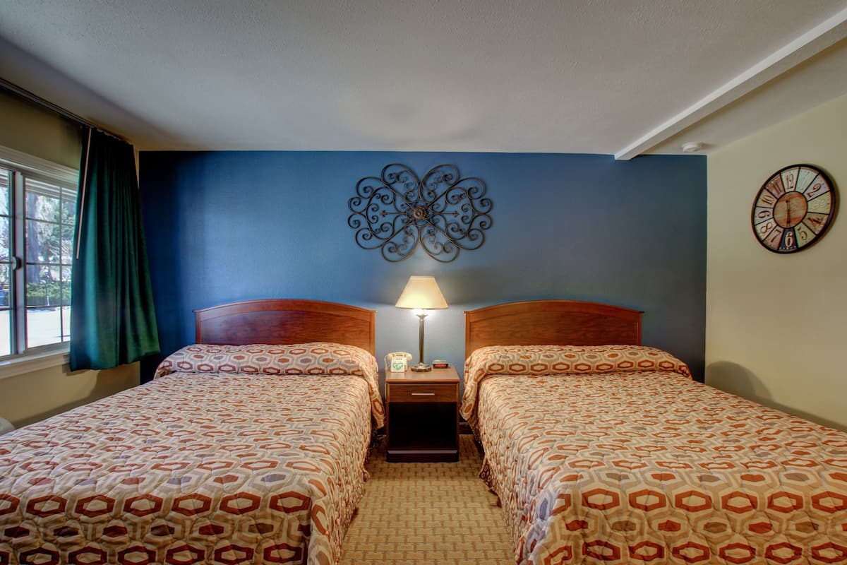 A hotel room with two beds, a nightstand with a lamp, a decorative wall piece, and a clock.
