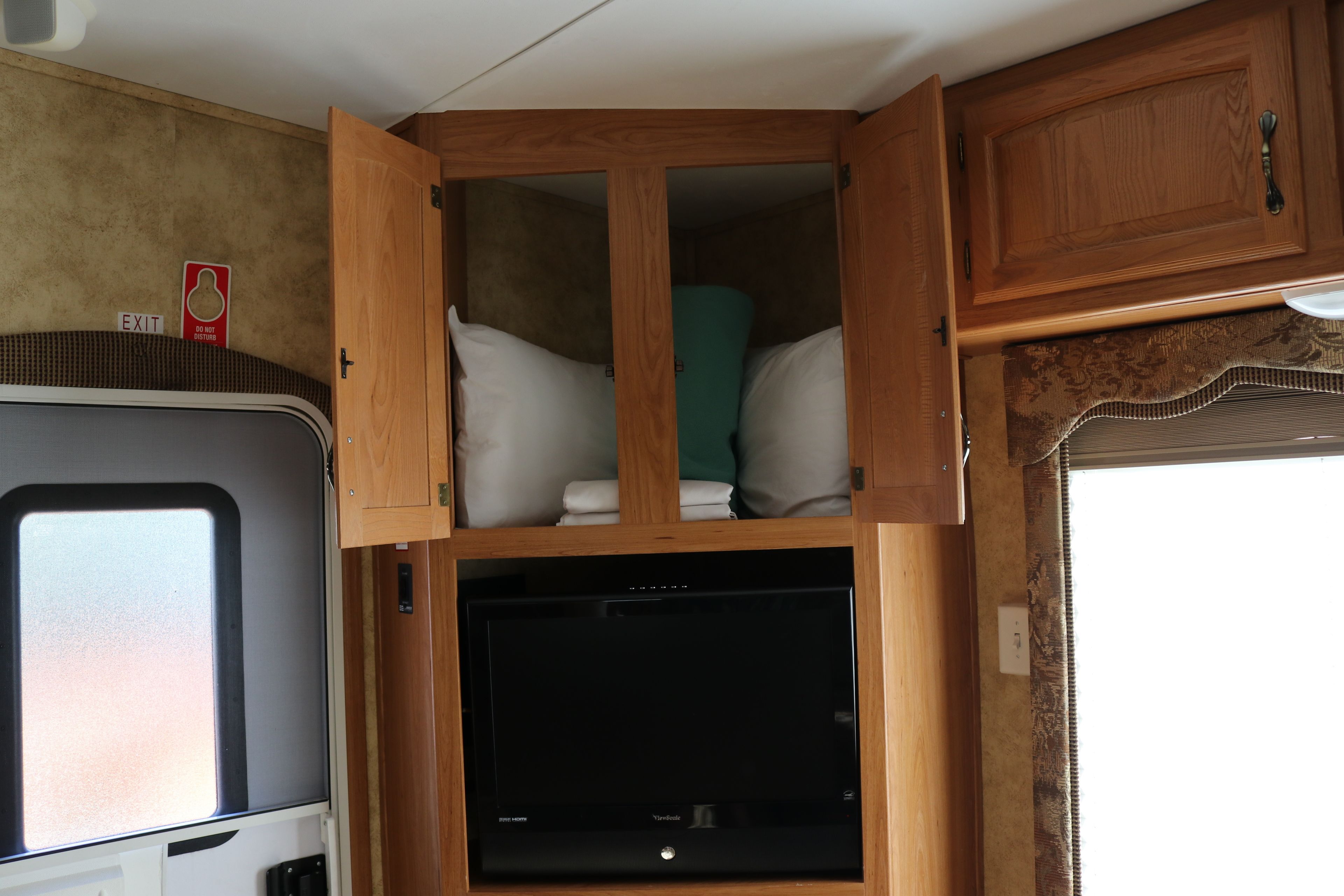 A compact RV interior with a TV, wooden cabinets, and a window.