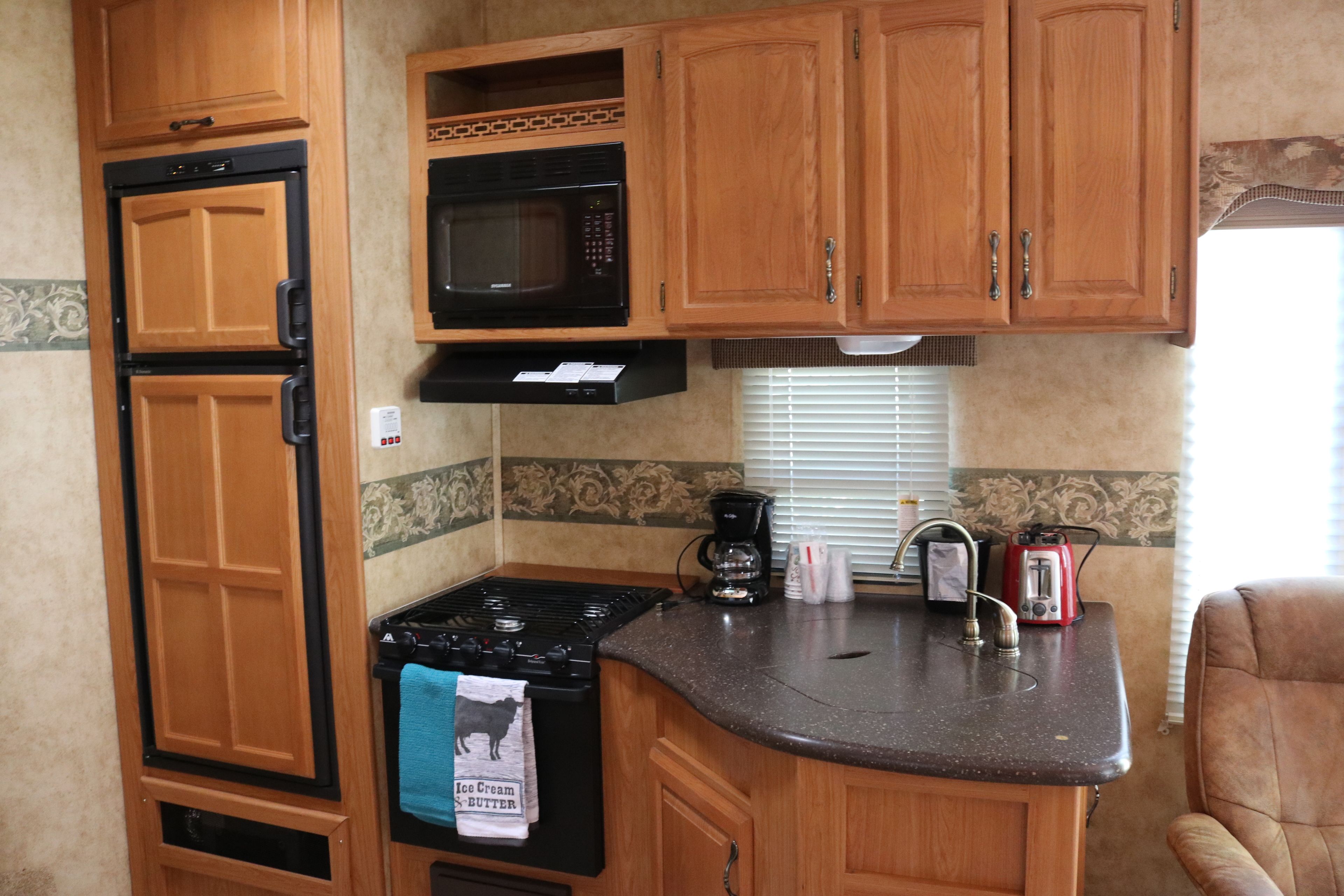 A compact kitchen with wooden cabinets, a built-in microwave, a stove, and a coffee maker.