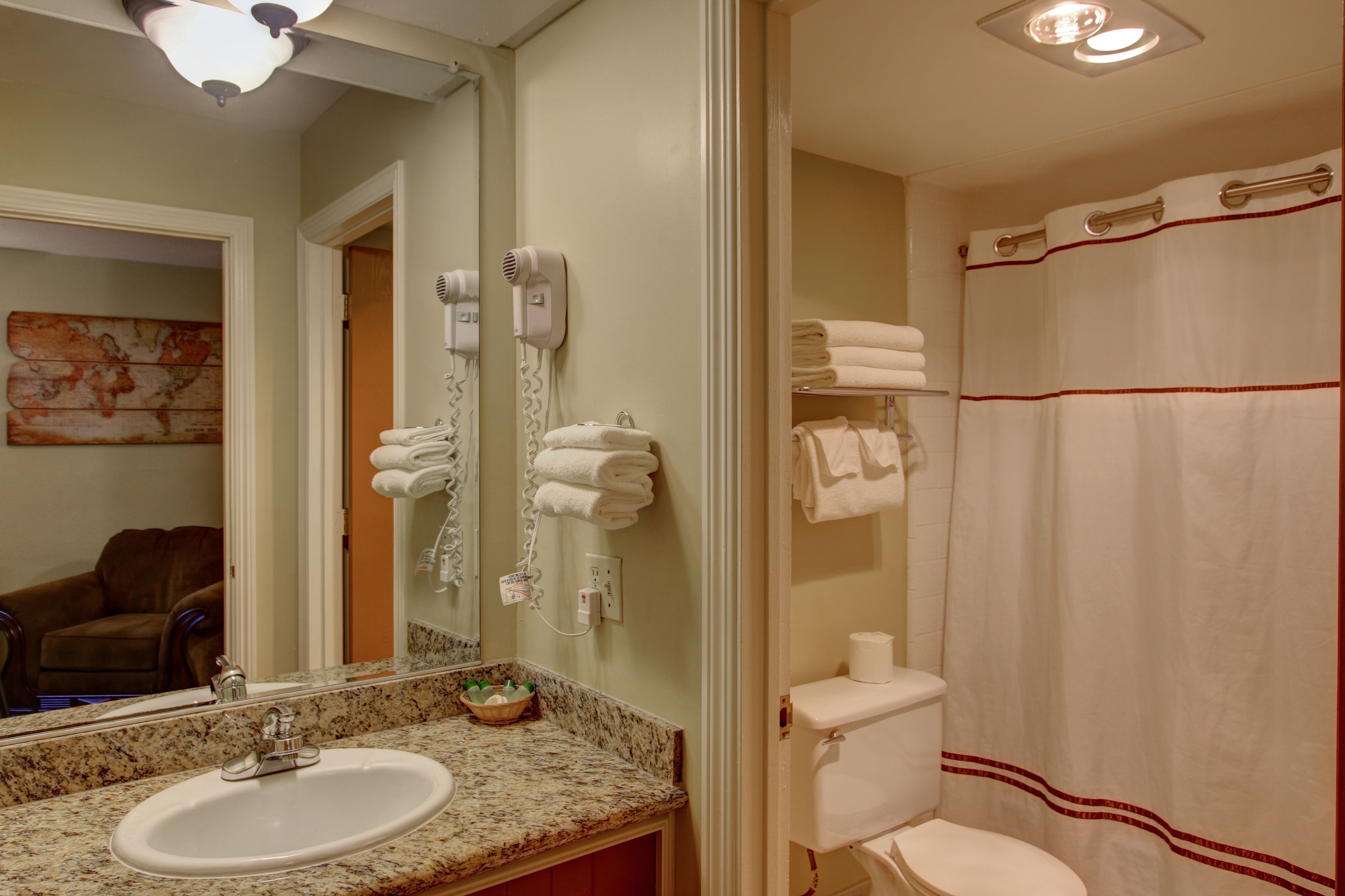 A bathroom with a sink, mirror, hairdryer, and toilet.