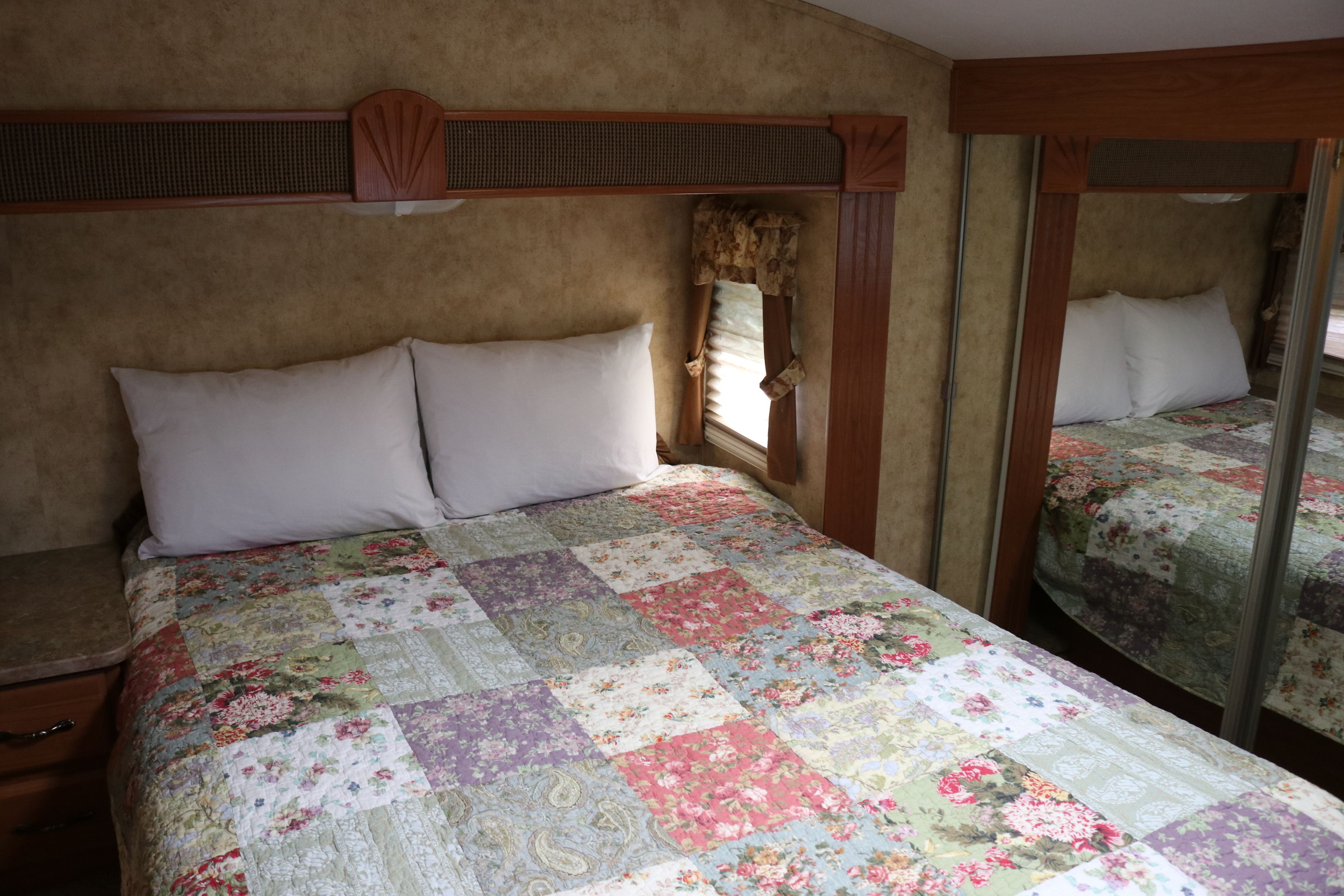 A bedroom with a large bed, a wooden headboard, a window with curtains, and a mirror on the wall.