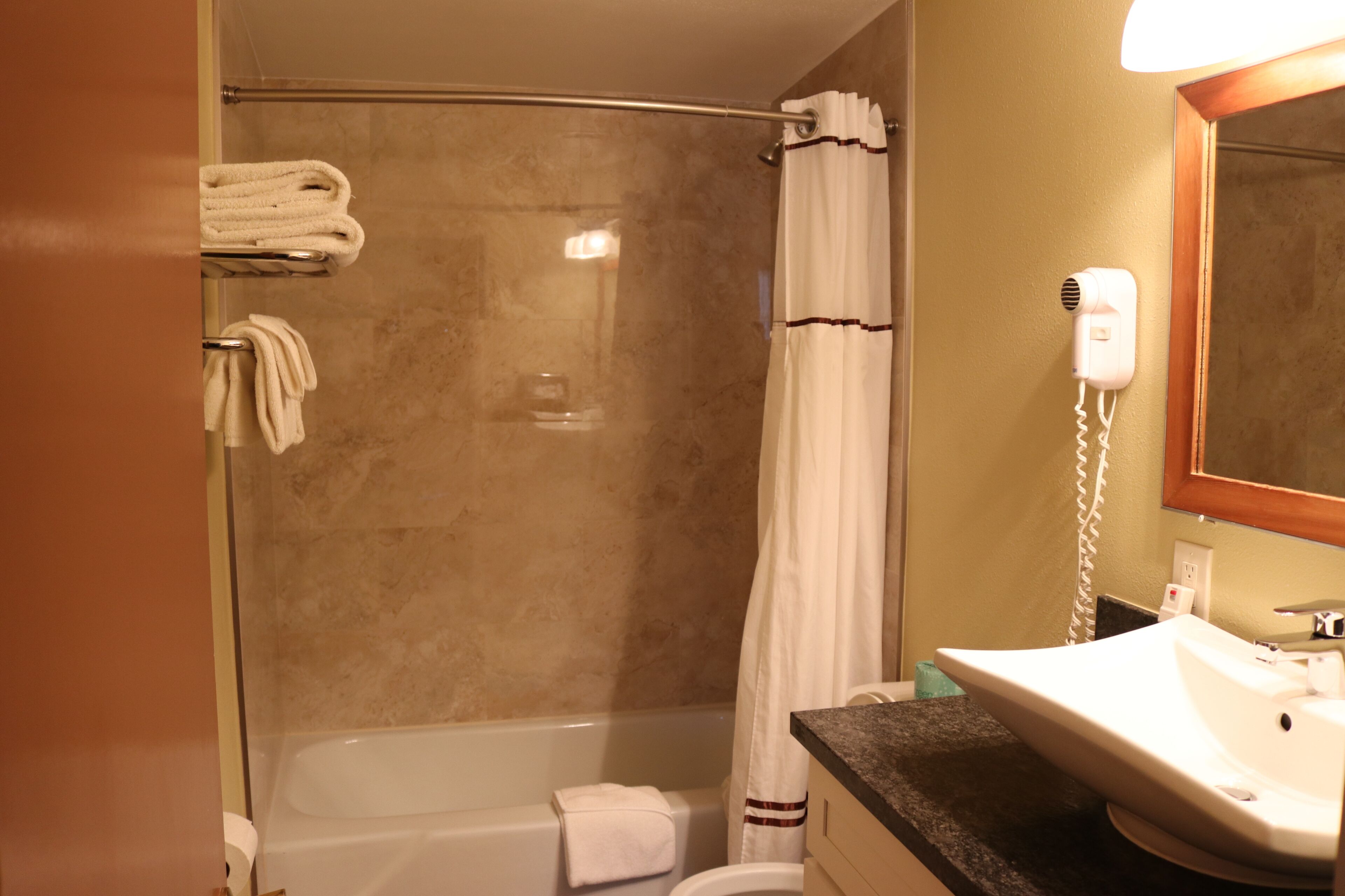 A bathroom with a glass-enclosed shower, a white sink, and a hairdryer mounted on the wall.