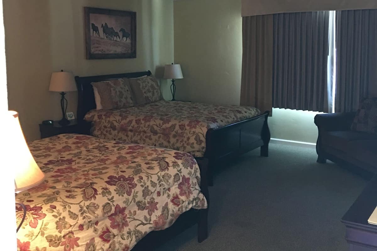 A hotel room with two beds, a chair, a lamp, and a painting on the wall.