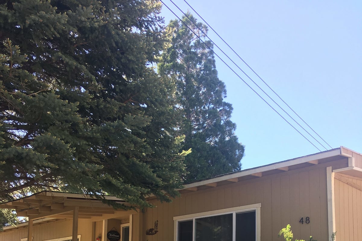 A two-story building with a beige exterior, a front porch with a staircase, and a small garden area.