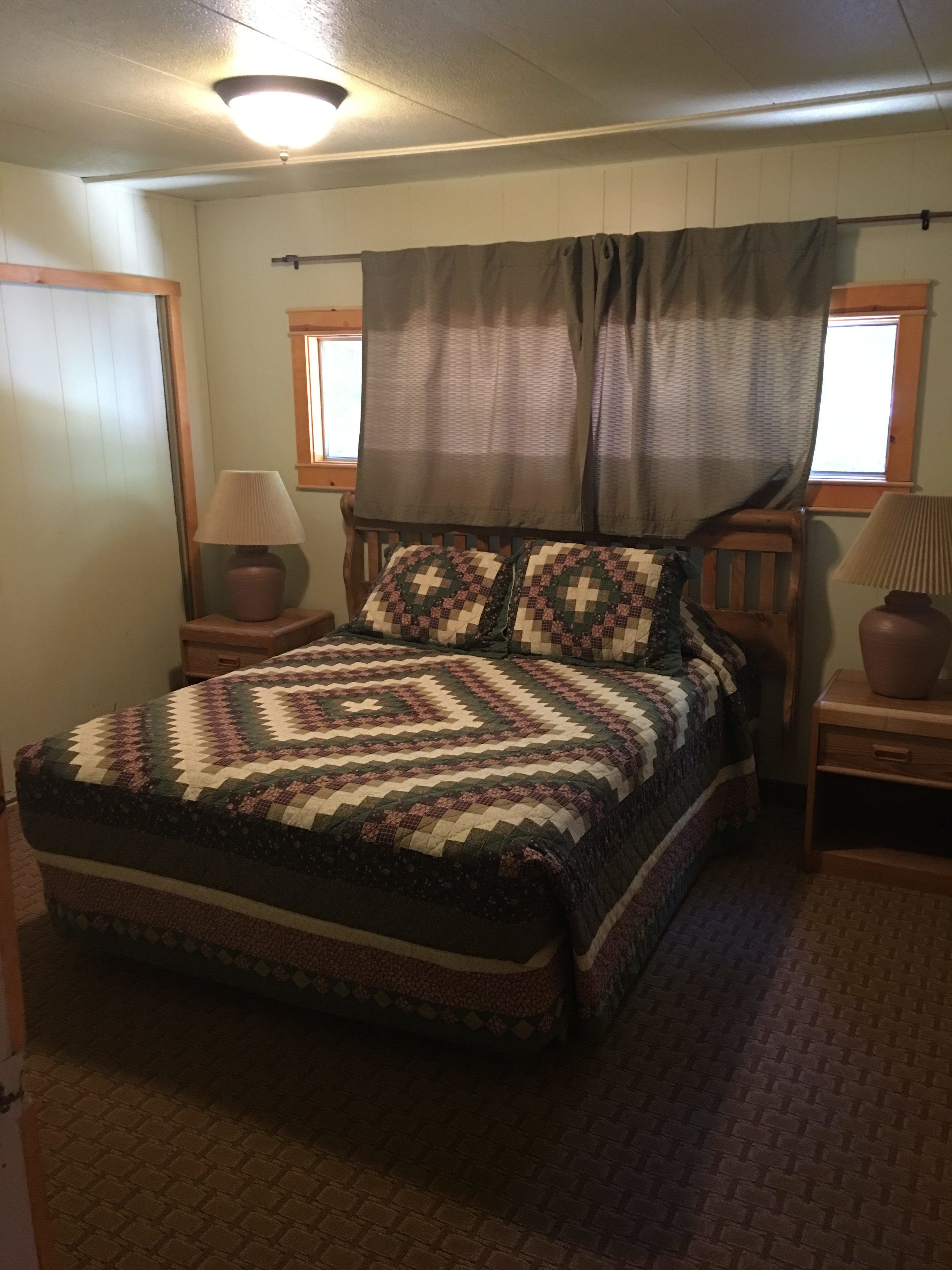 Quarto com cama, duas mesas de cabeceira, janela com cortinas e luminária no teto.