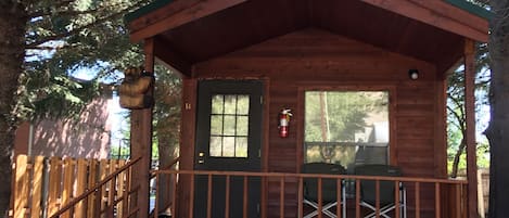 A small wooden cabin with a porch, a green door, and a window.