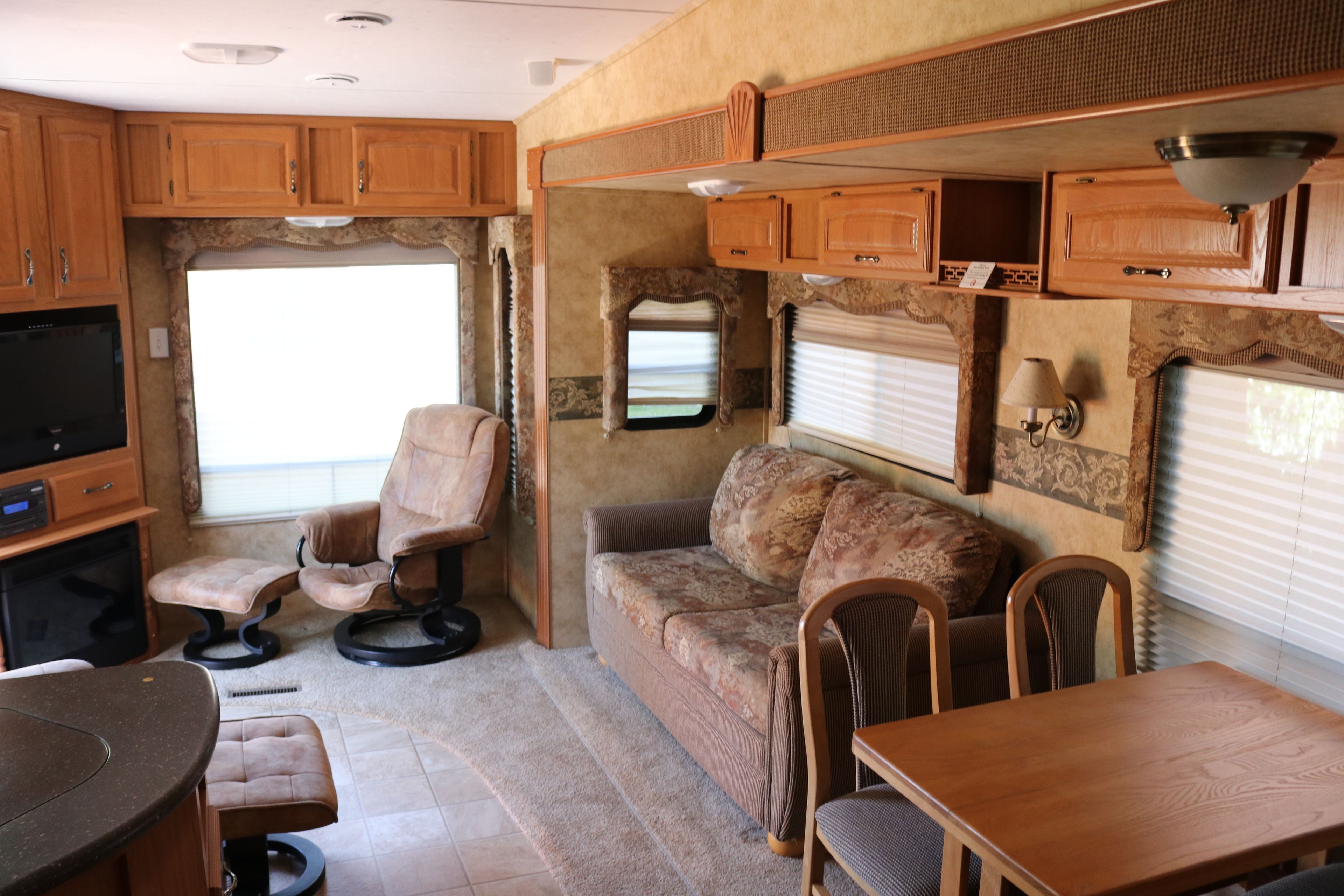Ein kompaktes Wohnmobil-Interieur mit einer Küchenzeile, einer Sitzecke, einem Esstisch und einem Fernseher.