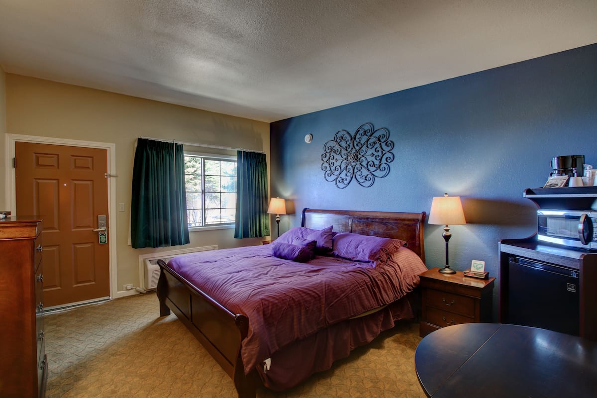 A bedroom with a bed, a dresser, a desk with a lamp, a coffee maker, and a microwave.