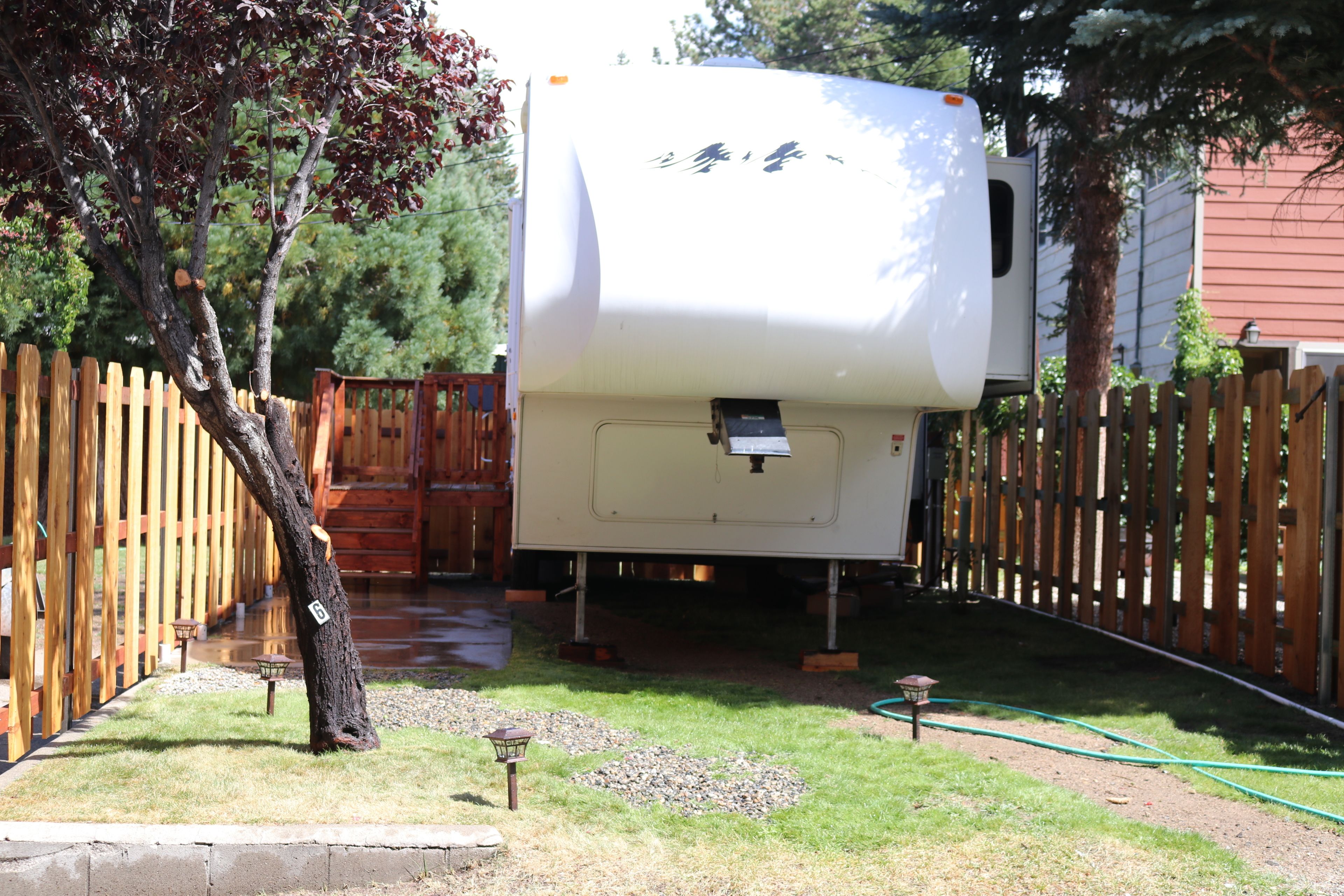 A white RV parked in a backyard with a wooden fence, a tree, and a garden area.