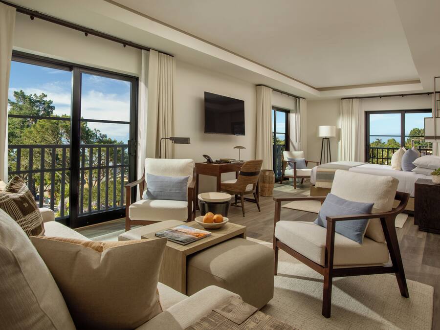 A spacious hotel room with a balcony, a flat-screen TV, a dining area, and a comfortable seating arrangement.