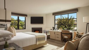 Une chambre d’hôtel moderne dotée d’un grand lit, d’un bureau, d’une cheminée et de grandes fenêtres donnant sur la forêt.