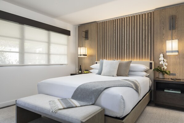 Una habitación de hotel moderna con una cama grande, lámparas de noche, una mesita de noche y una ventana con persianas.