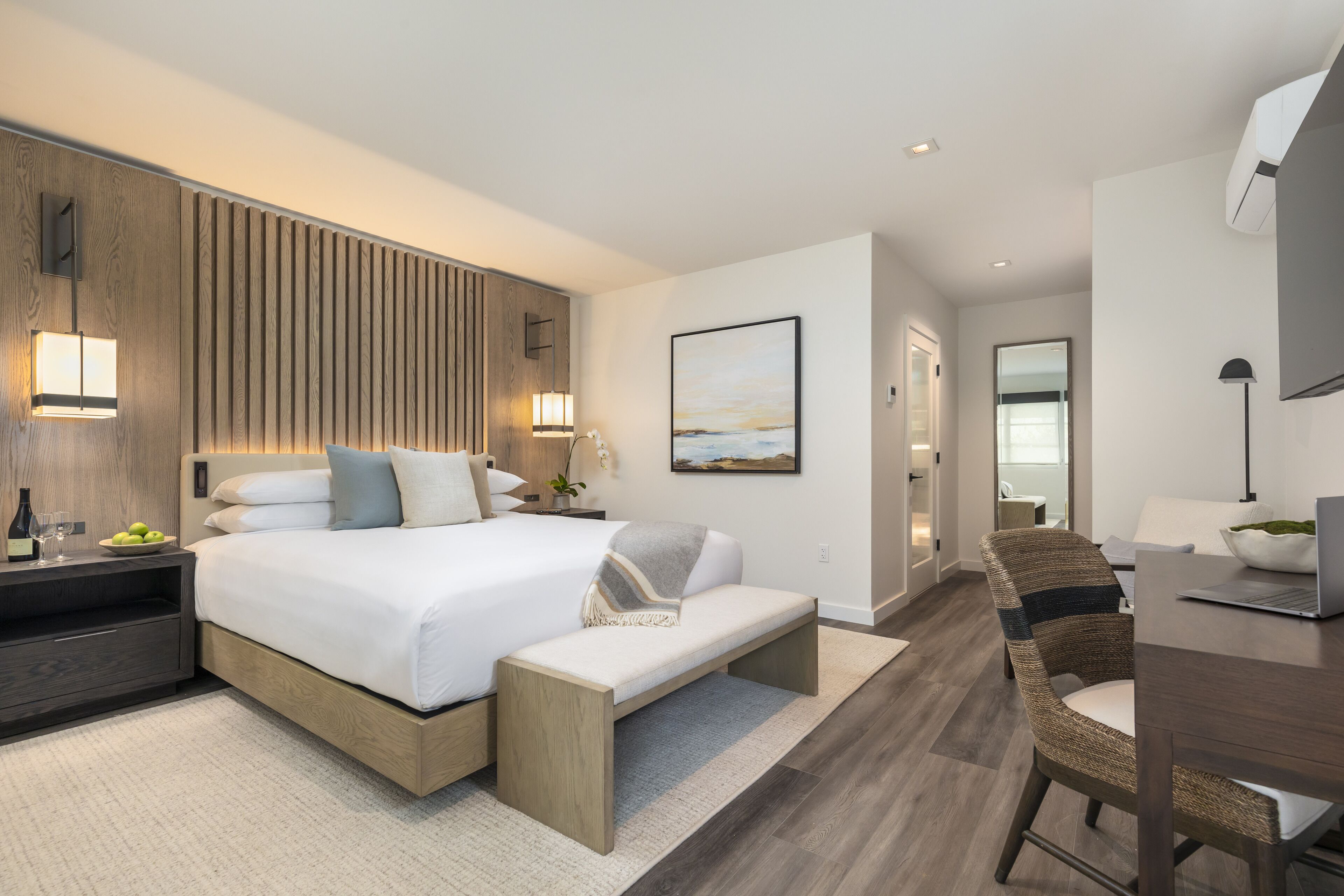 Een moderne slaapkamer met een groot bed, nachtkastjes, een bankje, een bureau en een stoel.