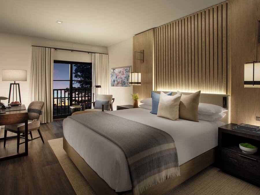 Habitación de hotel moderna con una cama grande, un escritorio, una silla y vistas al exterior.